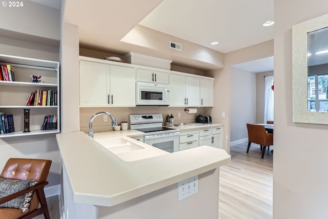 kitchen featuring white appliances, white cabinets, sink, light wood-type flooring, and kitchen peninsula