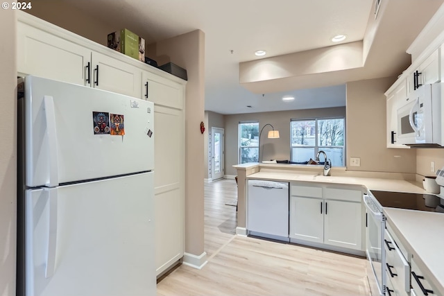 kitchen featuring white appliances, white cabinets, sink, light hardwood / wood-style floors, and kitchen peninsula