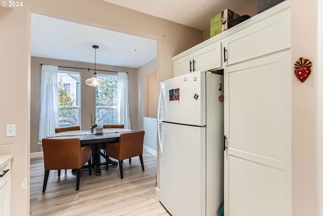 kitchen with white cabinets, decorative light fixtures, white fridge, and light hardwood / wood-style floors