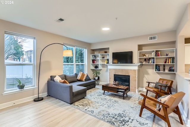 living room featuring a tiled fireplace, a wealth of natural light, and light wood-type flooring