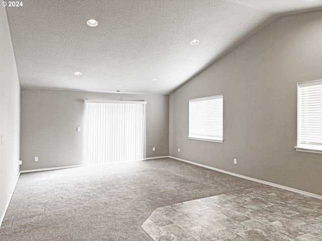 spare room with a textured ceiling, light colored carpet, and lofted ceiling