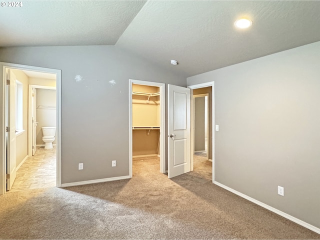 unfurnished bedroom with light carpet, a walk in closet, a textured ceiling, vaulted ceiling, and a closet