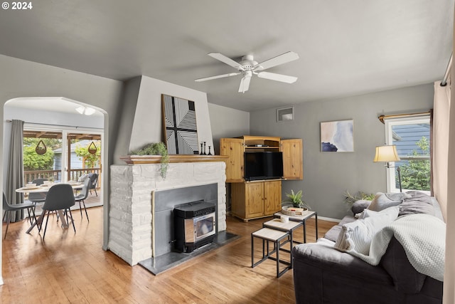 living room with a wealth of natural light, ceiling fan, a stone fireplace, and wood-type flooring