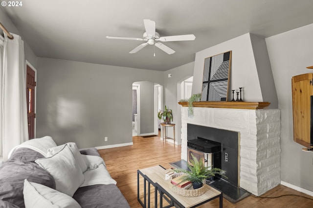 living room with wood-type flooring, ceiling fan, and a stone fireplace