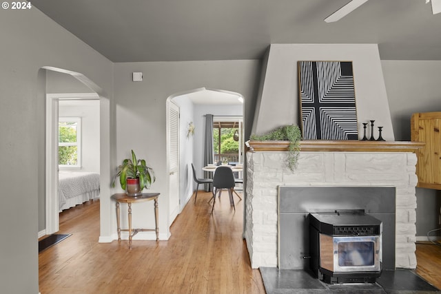 living room featuring wood-type flooring, ceiling fan, and a stone fireplace