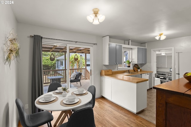 kitchen featuring white dishwasher, light wood-type flooring, sink, kitchen peninsula, and tasteful backsplash