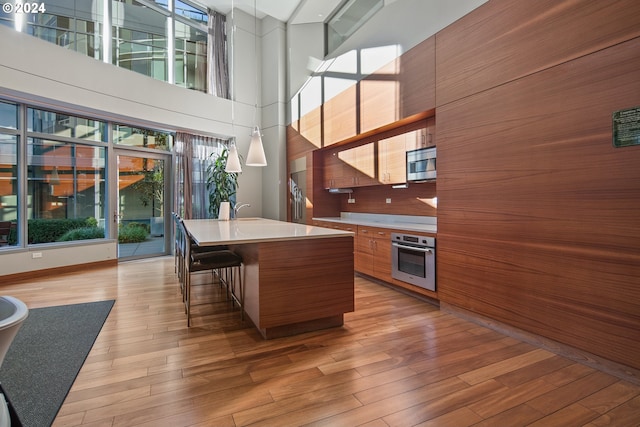 kitchen featuring appliances with stainless steel finishes, light hardwood / wood-style floors, a kitchen island with sink, and a high ceiling