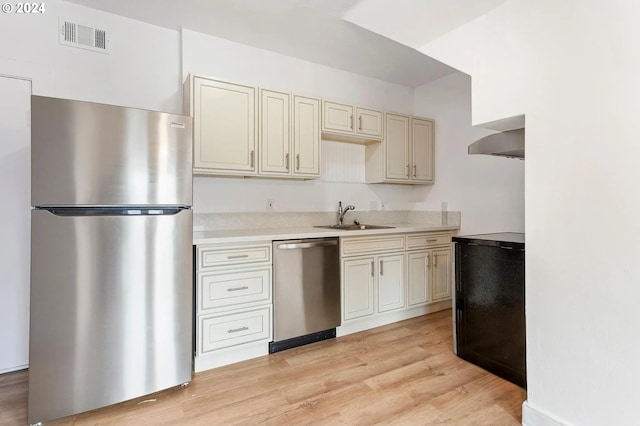 kitchen with appliances with stainless steel finishes, sink, light wood-type flooring, wall chimney range hood, and cream cabinetry