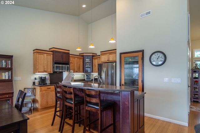 kitchen with dark countertops, light wood finished floors, visible vents, stainless steel appliances, and high vaulted ceiling