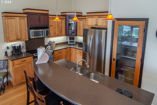 kitchen with light wood-type flooring, pendant lighting, a sink, dark countertops, and stainless steel appliances