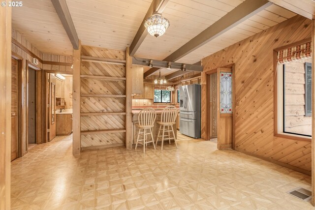 kitchen with stainless steel refrigerator with ice dispenser, a kitchen bar, wooden walls, kitchen peninsula, and beam ceiling