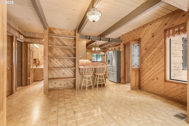 interior space with beamed ceiling, baseboards, wooden walls, and light floors