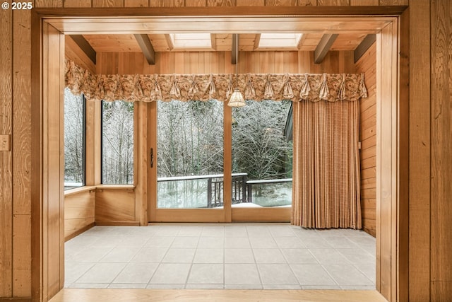 entryway with light tile patterned flooring, wooden walls, beamed ceiling, and a skylight