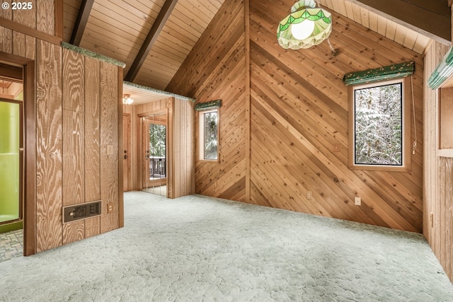 spare room featuring lofted ceiling with beams, a wealth of natural light, wood walls, and carpet floors