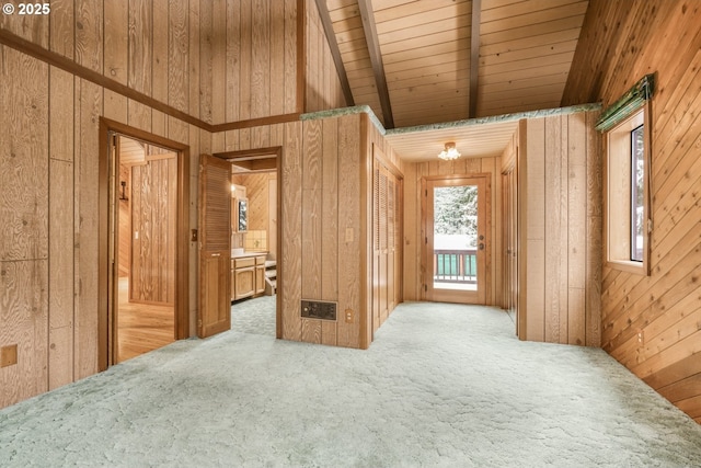 empty room featuring carpet floors, beam ceiling, wooden walls, and wooden ceiling