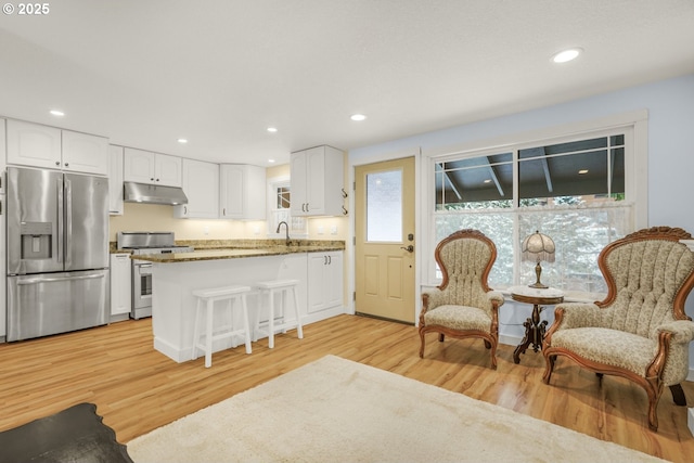 kitchen featuring appliances with stainless steel finishes, a breakfast bar area, white cabinets, kitchen peninsula, and light wood-type flooring