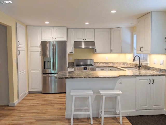 kitchen featuring gas stove, a peninsula, stainless steel fridge with ice dispenser, a sink, and under cabinet range hood