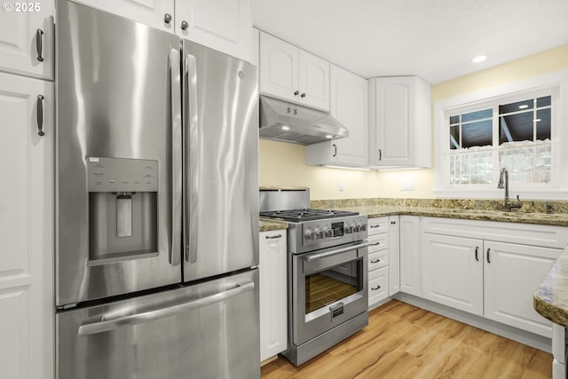 kitchen featuring stone countertops, a sink, white cabinets, under cabinet range hood, and appliances with stainless steel finishes