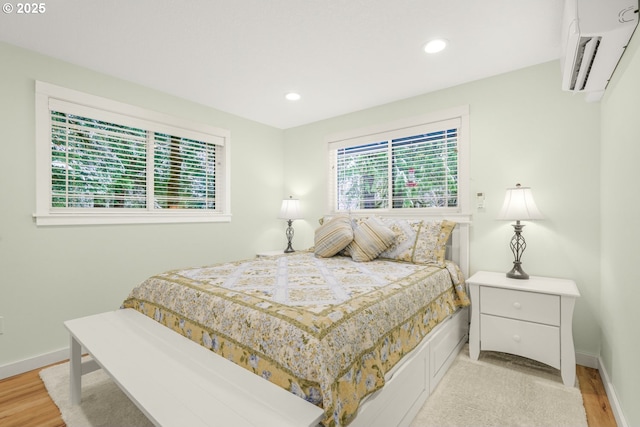 bedroom with a wall unit AC, recessed lighting, baseboards, and light wood finished floors