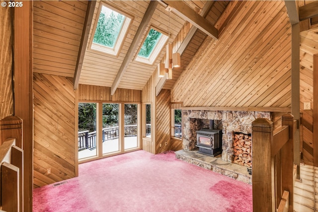 unfurnished living room featuring carpet floors, wooden walls, beamed ceiling, and a wood stove