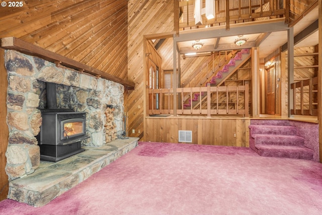 unfurnished living room featuring visible vents, carpet floors, wooden walls, and a wood stove