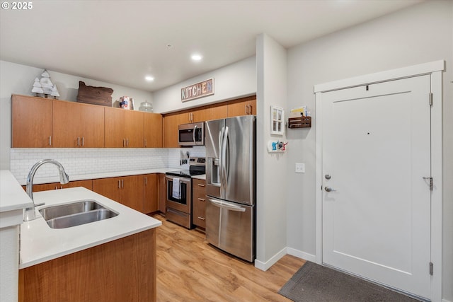 kitchen with appliances with stainless steel finishes, backsplash, light hardwood / wood-style floors, and sink