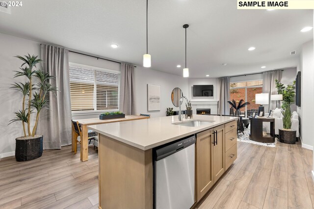 kitchen with light wood-type flooring, sink, stainless steel dishwasher, and a center island with sink