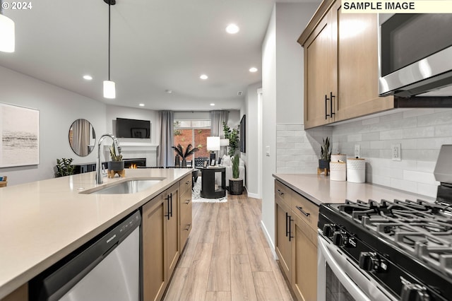 kitchen with appliances with stainless steel finishes, sink, backsplash, hanging light fixtures, and light hardwood / wood-style flooring