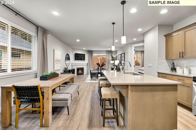 kitchen with light hardwood / wood-style floors, a kitchen island with sink, sink, and pendant lighting