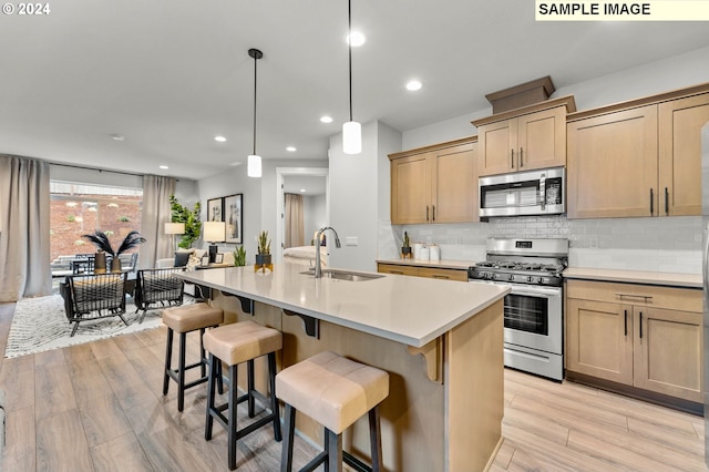 kitchen featuring appliances with stainless steel finishes, sink, light wood-type flooring, and an island with sink