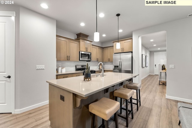 kitchen with sink, an island with sink, light wood-type flooring, stainless steel appliances, and decorative light fixtures