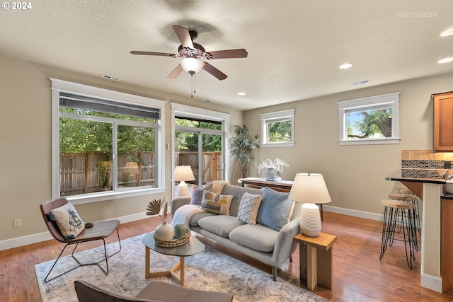 living room featuring ceiling fan, a textured ceiling, and light hardwood / wood-style flooring