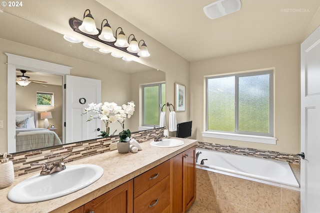 bathroom with decorative backsplash, tiled tub, ceiling fan, and dual bowl vanity