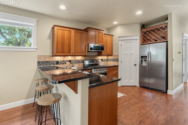 kitchen with appliances with stainless steel finishes, dark wood-type flooring, a kitchen breakfast bar, and tasteful backsplash