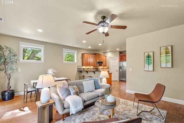 living room featuring light hardwood / wood-style floors, a textured ceiling, and ceiling fan