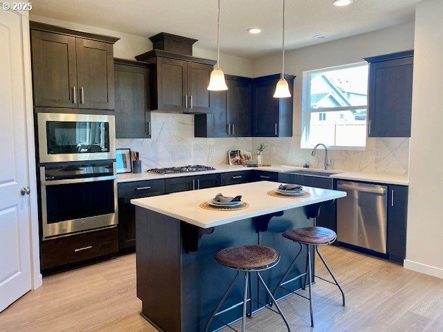 kitchen featuring light wood finished floors, light countertops, a sink, a breakfast bar, and appliances with stainless steel finishes