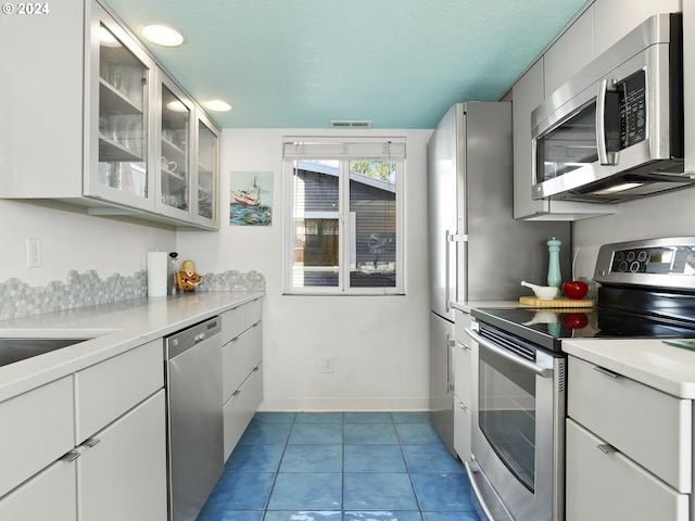 kitchen with tile flooring, white cabinets, stainless steel appliances, and a textured ceiling