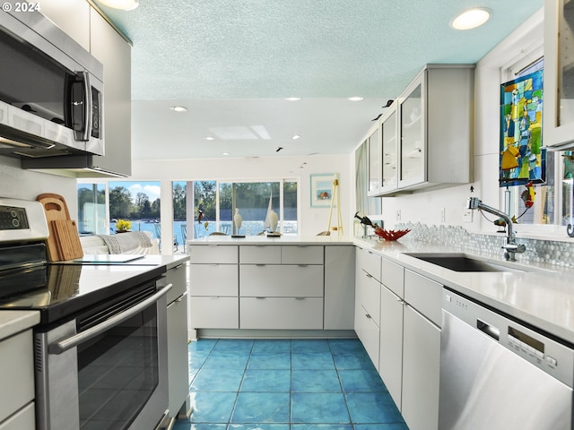 kitchen with light tile flooring, white cabinetry, stainless steel appliances, sink, and a textured ceiling