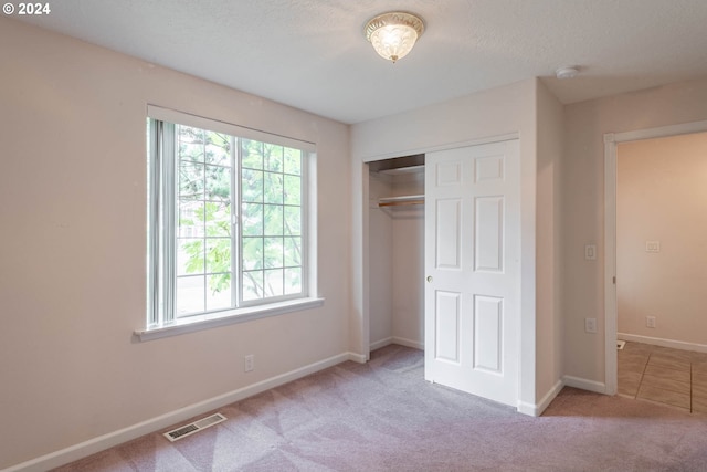 unfurnished bedroom featuring a textured ceiling, light carpet, and a closet