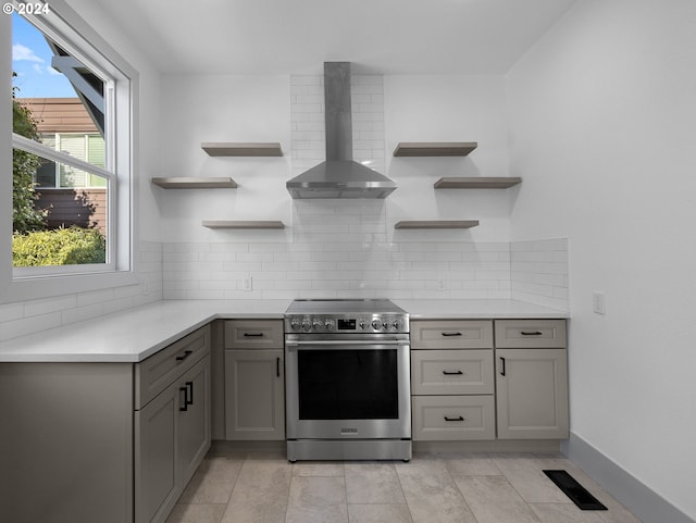 kitchen with gray cabinets, wall chimney exhaust hood, decorative backsplash, and stainless steel electric range oven