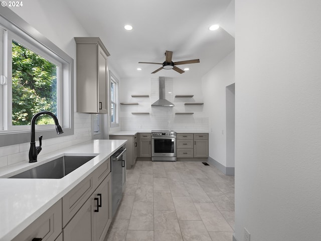 kitchen with wall chimney exhaust hood, gray cabinetry, sink, appliances with stainless steel finishes, and tasteful backsplash