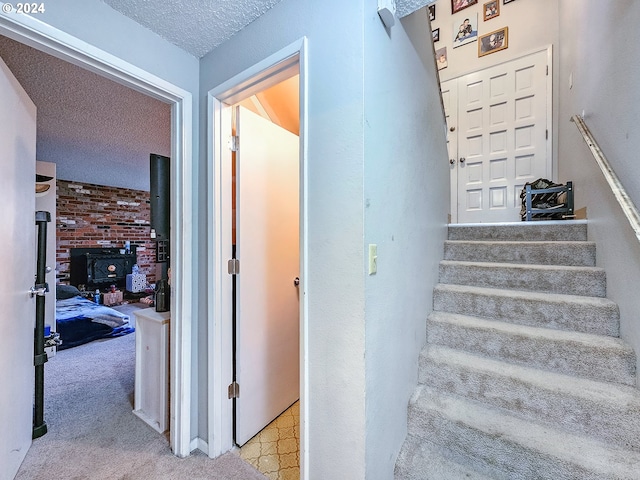 staircase with a wood stove, light colored carpet, and a textured ceiling