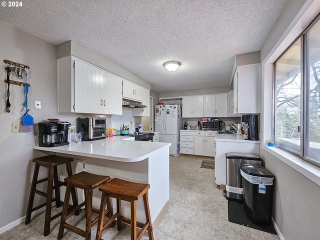 kitchen with light tile floors, kitchen peninsula, a breakfast bar, white refrigerator, and white cabinetry