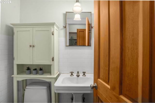 bathroom featuring toilet, sink, and tile walls