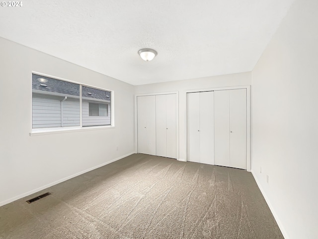 unfurnished bedroom featuring multiple closets, carpet floors, and a textured ceiling