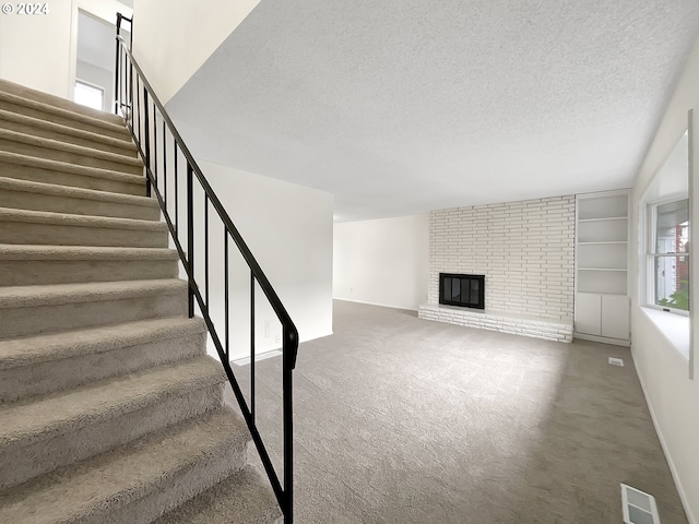 stairway with a fireplace, a textured ceiling, and carpet floors