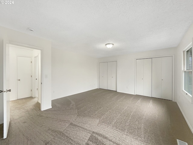 unfurnished bedroom featuring two closets, a textured ceiling, and carpet floors