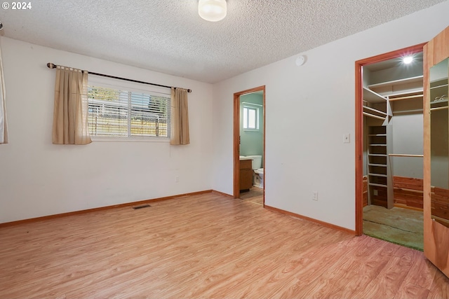 unfurnished bedroom with a spacious closet, a textured ceiling, a closet, and light wood-type flooring