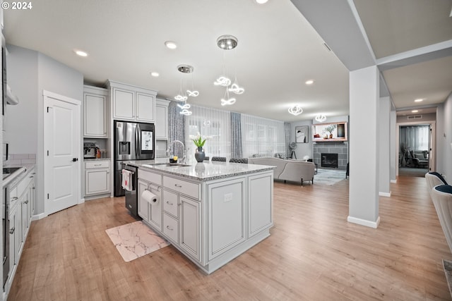 kitchen featuring pendant lighting, light hardwood / wood-style floors, sink, a tiled fireplace, and a center island with sink