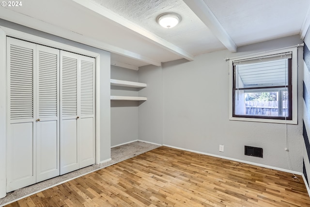 unfurnished bedroom featuring a textured ceiling, light hardwood / wood-style floors, a closet, and beamed ceiling